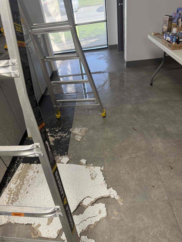 Responded to an emergency service call for commercial water leak at pharmacy following previous day's repair. Discovered significant water pooling on concrete floor with ceiling material debris present. Inspection revealed leak source in ceiling area above office workspace, requiring ladder access for complete repair and water extraction to prevent further damage to facility.