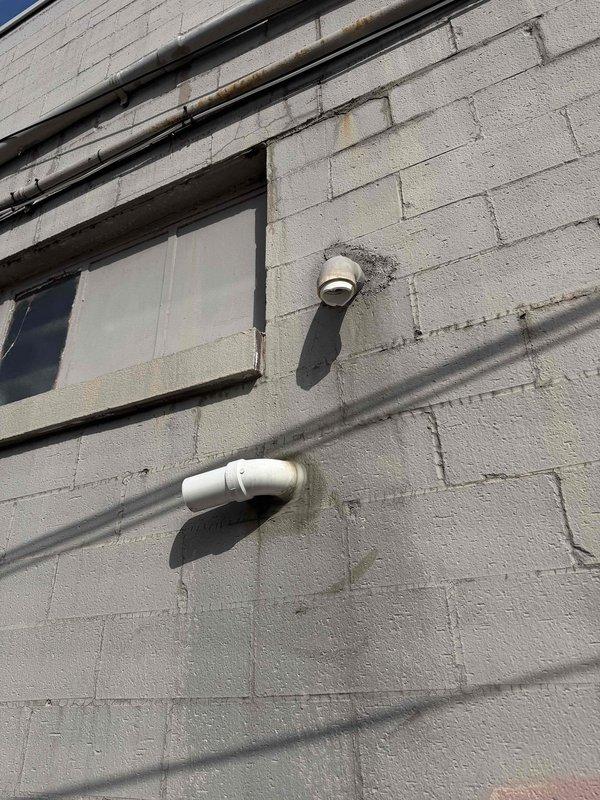 Responded to no-heat callback from previous day's service. Upon arrival, the heating system was operational but discovered water leakage around the unit affecting both the customer's premises and the adjacent business. Inspection revealed moisture damage and staining around exterior wall penetrations where HVAC condensate lines exit the building, specifically at PVC pipe connections.