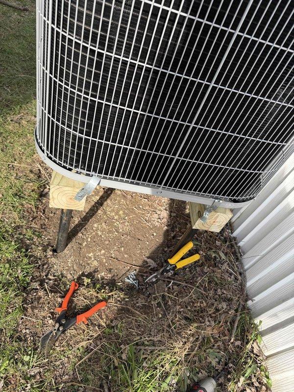 Completed warranty follow-up on outdoor HVAC condenser unit to address mounting stability concerns. Inspected unit positioning on wooden support platform and verified secure attachment to prevent movement or shifting. Unit is properly elevated on pressure-treated lumber base with adequate clearance from ground surface for drainage and airflow.