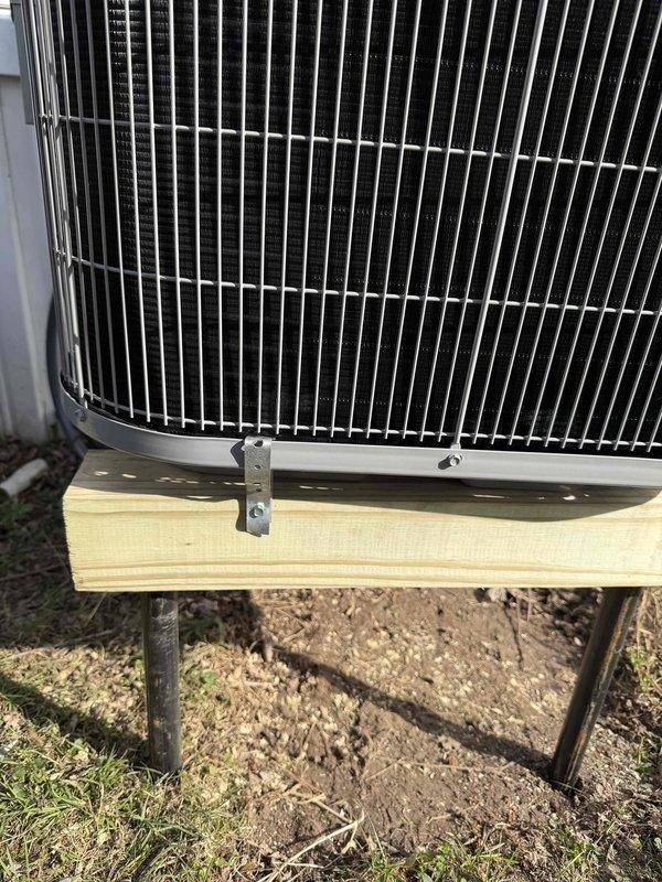 Completed warranty follow-up on outdoor HVAC condenser unit to address mounting stability concerns. Inspected unit positioning on wooden support platform and verified secure attachment to prevent movement or shifting. Unit is properly elevated on pressure-treated lumber base with adequate clearance from ground surface for drainage and airflow.