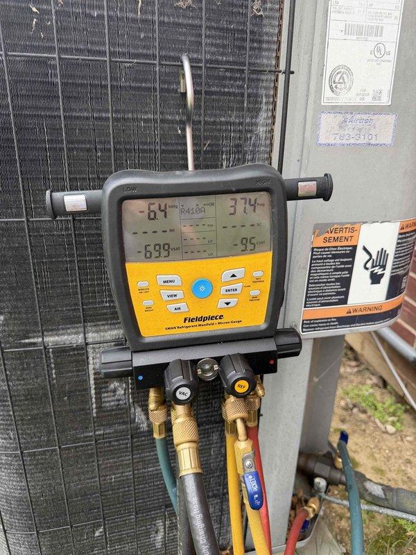 Responded to no cooling call at new location. Upon arrival, performed system diagnostics using digital manifold gauges on outdoor condensing unit. Measured operating pressures and temperatures, with readings indicating 64°F and 37.4°F across the system. Inspected outdoor unit cabinet and internal components, finding condenser coil in clean condition with no visible obstructions. Also inspected indoor equipment located in basement utility area, noting water heater installation with copper piping connections. Observed mineral deposits and white crystalline buildup on surface near plumbing equipment, though this appeared related to separate water system issue rather than HVAC malfunction. Completed refrigerant pressure analysis and temperature differential measurements to diagnose cooling system performance. All safety labels and manufacturer information verified present on equipment.