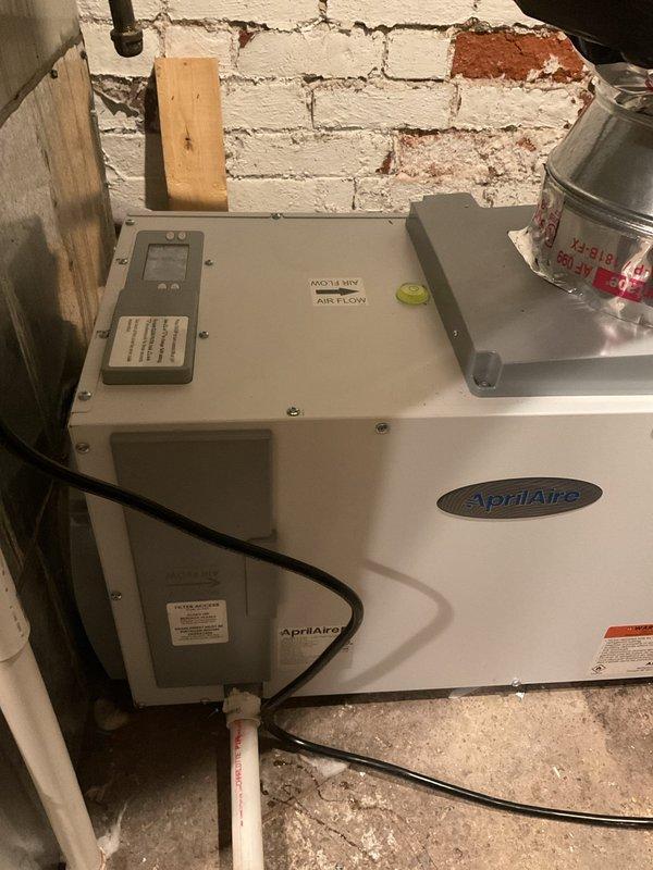 Installed AprilAire whole-home dehumidifier unit in basement utility area. Connected unit to existing HVAC system with metallic flex ductwork, established condensate drainage via yellow corrugated drain line to existing PVC drain system, and completed electrical wiring connections. Unit was tested and verified operational upon completion.