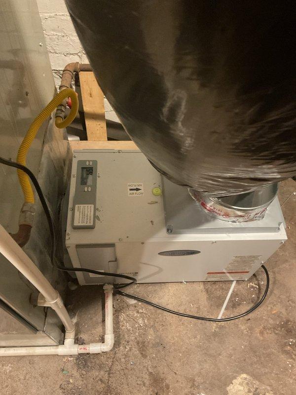 Installed AprilAire whole-home dehumidifier unit in basement utility area. Connected unit to existing HVAC system with metallic flex ductwork, established condensate drainage via yellow corrugated drain line to existing PVC drain system, and completed electrical wiring connections. Unit was tested and verified operational upon completion.