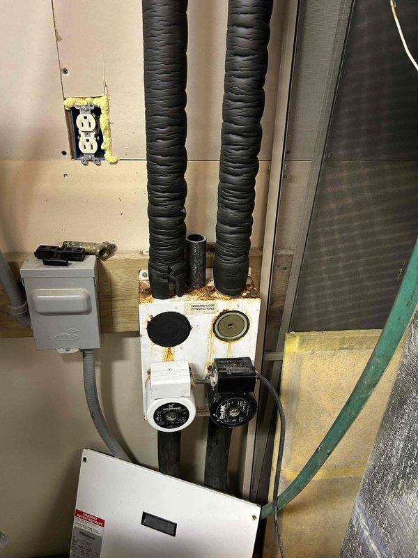 Conducted comprehensive assessment of 25-year-old ClimateMaster WaterFurnace Premier geothermal heat pump system for replacement evaluation. Unit exhibited age-related deterioration including surface corrosion on mounting hardware, rust staining around connection points, and general wear consistent with extended service life. Documented existing installation configuration including black flexible ductwork connections, electrical service components, and mechanical room layout. Photographed unit specifications, service history labels, and existing infrastructure to develop accurate replacement proposal for new geothermal system.