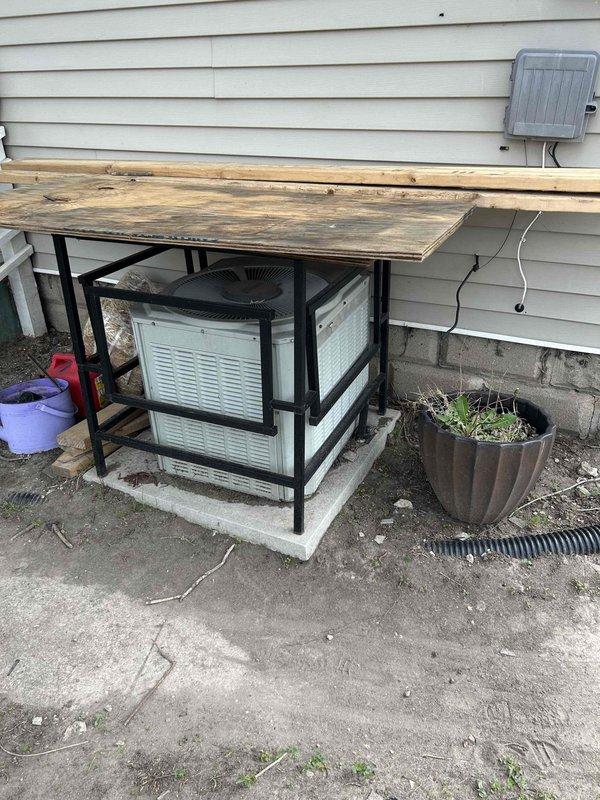 Conducted comprehensive site evaluation for complete HVAC system replacement at residential property. Assessed existing outdoor Carrier air conditioning condenser unit housed in protective cage enclosure, noting aged wooden platform cover and concrete pad installation. Documented current equipment positioning against exterior wall with vinyl siding, electrical conduit routing, and outdoor disconnect box location. Evaluated basement furnace installation including existing ductwork configuration with insulated supply plenum and flexible duct connections. Photographed mechanical room layout, concrete foundation walls, and current equipment clearances for replacement planning. Provided estimate for new complete system installation including outdoor condensing unit and indoor air handler or furnace replacement with necessary electrical, refrigerant line set, and ductwork modifications as required.