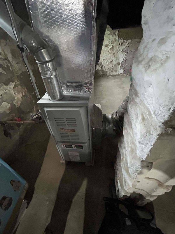 Conducted comprehensive site evaluation for complete HVAC system replacement at residential property. Assessed existing outdoor Carrier air conditioning condenser unit housed in protective cage enclosure, noting aged wooden platform cover and concrete pad installation. Documented current equipment positioning against exterior wall with vinyl siding, electrical conduit routing, and outdoor disconnect box location. Evaluated basement furnace installation including existing ductwork configuration with insulated supply plenum and flexible duct connections. Photographed mechanical room layout, concrete foundation walls, and current equipment clearances for replacement planning. Provided estimate for new complete system installation including outdoor condensing unit and indoor air handler or furnace replacement with necessary electrical, refrigerant line set, and ductwork modifications as required.