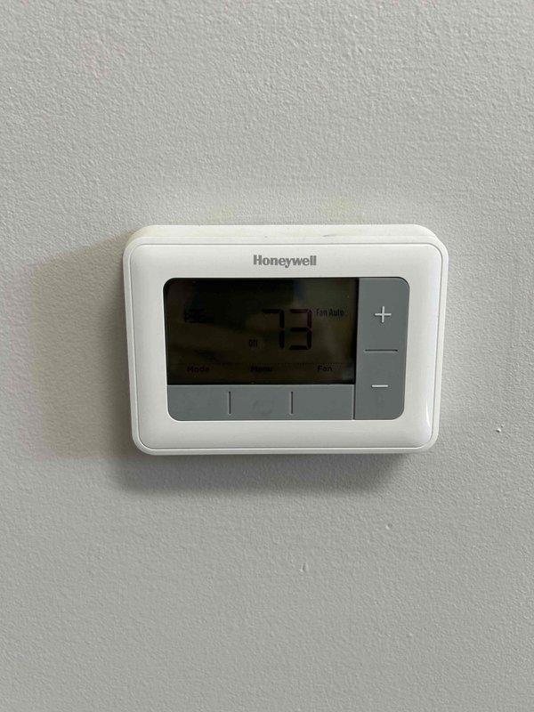 Conducted comprehensive site evaluation for complete HVAC system replacement in total electric home serviced by AES utility provider. Assessed existing electrical infrastructure including main service panel with dual-row circuit breaker configuration and current Honeywell digital thermostat displaying 73°F ambient temperature. Documented electrical service capacity, available breaker positions, and compatibility requirements for new all-electric heating and cooling equipment installation.