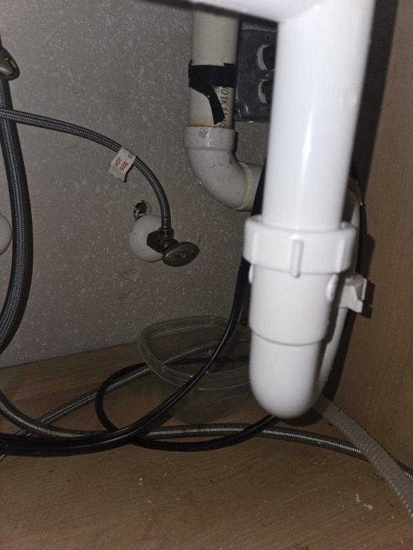Responded to service call for two dripping shut-off valves located beneath bathroom sink. Upon arrival, accessed property using lockbox and inspected plumbing installation in cabinet space. Documented existing conditions showing chrome-plated angle stop valves with oval handles connected to braided flexible supply lines. Photographed both affected valves and surrounding plumbing components including PVC drain assembly and water supply connections to establish baseline conditions for repair assessment.