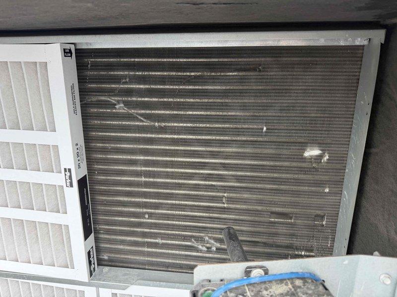 Performed diagnostic evaluation on two commercial HVAC units experiencing cooling failures. First unit servicing cafe area exhibited no cool air output; inspection revealed suspected evaporator coil leak requiring further assessment. Second unit, a Carrier WeatherMaker rooftop package unit, displayed abnormal amperage readings and heavily soiled condenser coils compromising heat rejection efficiency. Documented equipment conditions with photographic evidence showing indoor evaporator assembly with air filter in place and rooftop unit with visible water pooling around base. Recommended comprehensive repair quote for both units including evaporator coil replacement or repair on first system and condenser coil cleaning with electrical diagnostics on second unit, along with proposed four-visit annual maintenance agreement to prevent future failures.