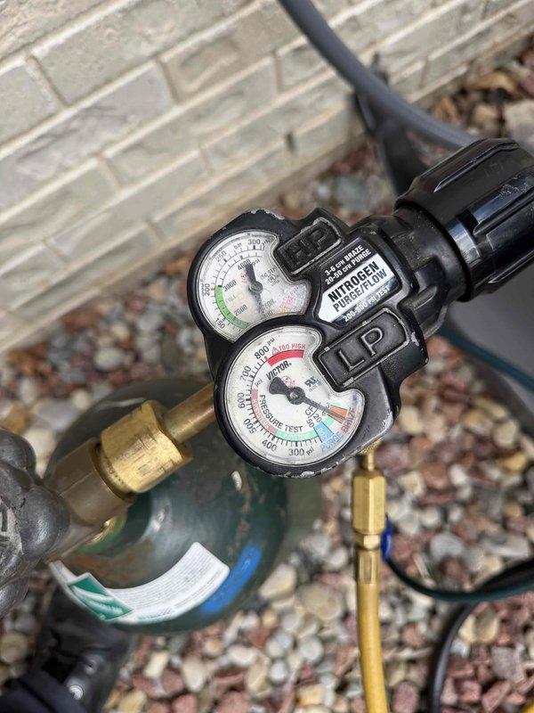 Responded to warranty service call for one-year-old HVAC system with reported lack of temperature change. Upon arrival, performed comprehensive system diagnostics on garage-installed furnace and air handler unit. Conducted pressure testing using nitrogen test equipment to verify refrigerant charge levels and identify potential leaks in the system. Measurements indicated system pressures were outside normal operating parameters. Inspected all refrigerant lines, connections, and components for leaks or damage. Verified proper electrical connections and control wiring integrity throughout the system. Checked condensate drain lines and PVC piping for proper drainage and blockages. System restored to proper operating condition with correct refrigerant pressures established and all components functioning within manufacturer specifications.