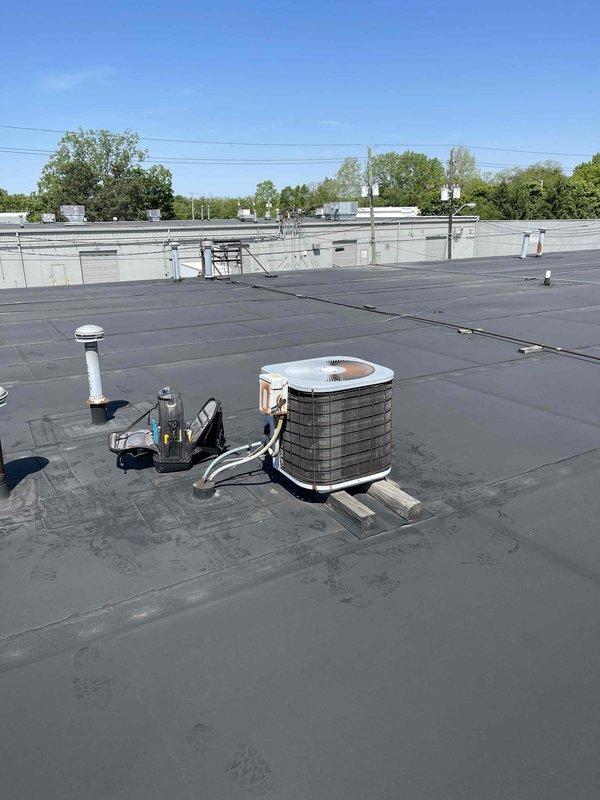 Responded to no cooling complaint on commercial rooftop unit accessible by ladder. Accessed RTU on flat roof membrane and inspected cylindrical condenser unit, refrigerant lines, and electrical connections. Documented rooftop equipment configuration including ductwork, air handler, control box, and associated mechanical systems in attic space for diagnostic assessment.
