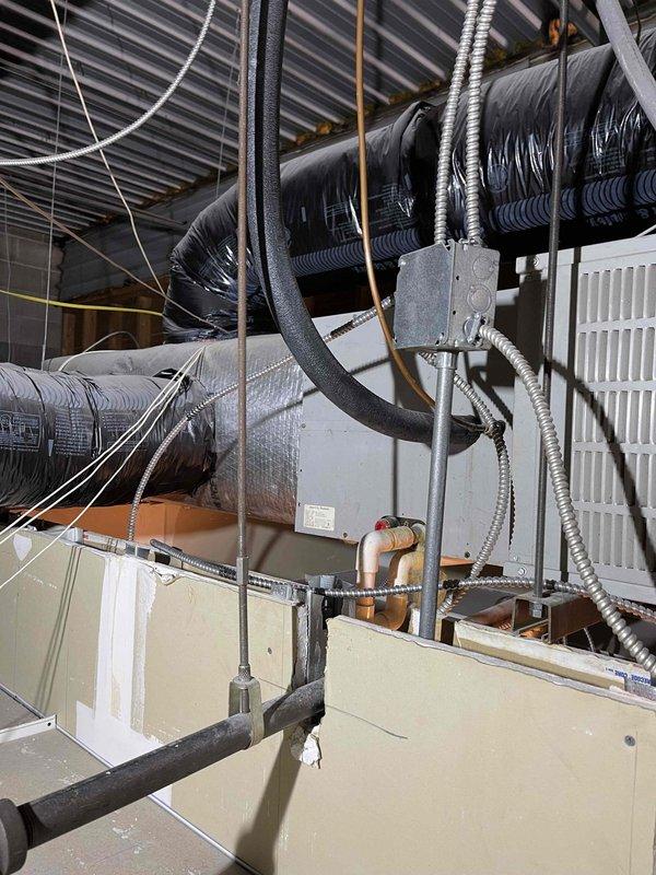 Responded to no cooling complaint on commercial rooftop unit accessible by ladder. Accessed RTU on flat roof membrane and inspected cylindrical condenser unit, refrigerant lines, and electrical connections. Documented rooftop equipment configuration including ductwork, air handler, control box, and associated mechanical systems in attic space for diagnostic assessment.