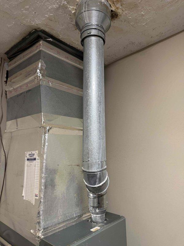 Performed inspection of furnace flue pipe system following home inspection report indicating corrosion concerns. Upon examination, confirmed significant deterioration of galvanized metal flue pipe elbow joint and vertical sections, with visible surface corrosion, discoloration, and aging throughout the exhaust system. The 90-degree elbow connection showed advanced wear with accumulated grime and oxidation at seams and fastener points. Documented condition of flue pipe penetration through ceiling and overall furnace installation. Provided homeowner with assessment findings and repair recommendations to address corroded flue pipe components prior to property sale closing.