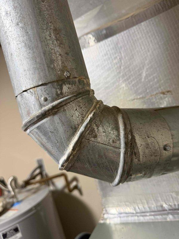 Performed inspection of furnace flue pipe system following home inspection report indicating corrosion concerns. Upon examination, confirmed significant deterioration of galvanized metal flue pipe elbow joint and vertical sections, with visible surface corrosion, discoloration, and aging throughout the exhaust system. The 90-degree elbow connection showed advanced wear with accumulated grime and oxidation at seams and fastener points. Documented condition of flue pipe penetration through ceiling and overall furnace installation. Provided homeowner with assessment findings and repair recommendations to address corroded flue pipe components prior to property sale closing.