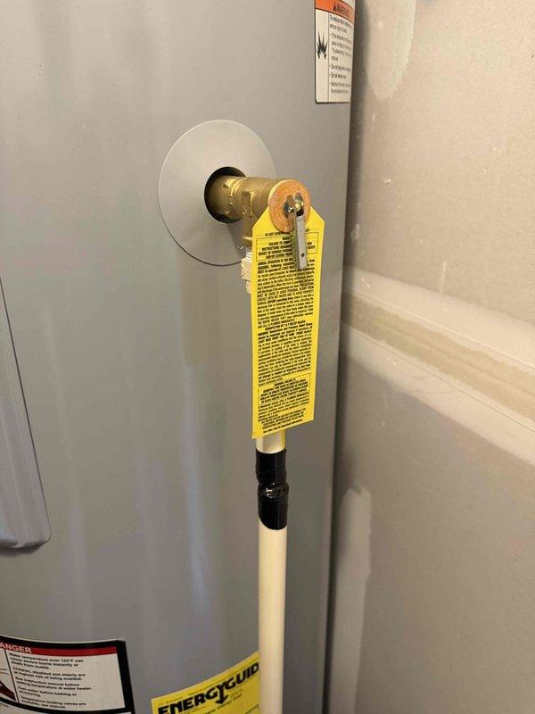 Responded to water leak complaint on recently installed water softener system. Upon arrival, inspected the unit and surrounding plumbing connections for signs of overflow or leakage. Verified all shut-off valves, supply lines, and drain connections were properly secured and functioning. Documented equipment condition and installation setup with photographs showing water heater, brass shut-off valve assembly with escutcheon plate, and utility area configuration. Addressed overflow issue and ensured proper drainage to prevent future water spillage on floor.