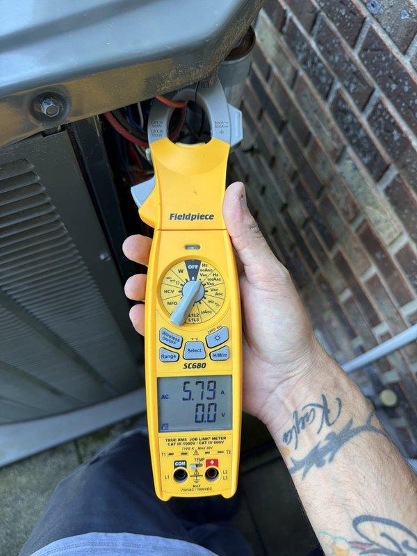 Completed routine maintenance inspection on residential cooling system. Performed visual assessment of outdoor condenser unit, confirmed fan assembly and protective grille in proper working condition, and conducted electrical diagnostics using clamp meter to verify amperage draw of 5.79 amps, indicating normal operating parameters for the compressor circuit.