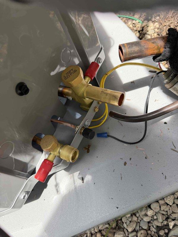 Completed full HVAC system installation with outdoor condensing unit mounted on concrete pad. Installed refrigeration line set with brass service valves, soldered copper piping connections, and wired electronically-controlled solenoid valves with proper electrical connections. All service ports capped, system secured to mounting platform, and refrigerant lines properly connected and ready for system startup and commissioning.