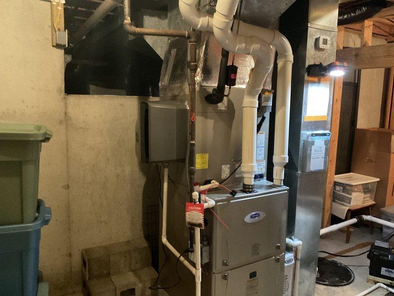 Completed full HVAC system installation in residential basement mechanical room. Installed new Carrier furnace unit with proper venting using white PVC piping routed vertically through ceiling joists, copper refrigerant lines, and electrical connections to existing panel. Configured supply and return ductwork with galvanized steel plenum connections to distribute conditioned air throughout residence. All components tested and verified operational upon completion.