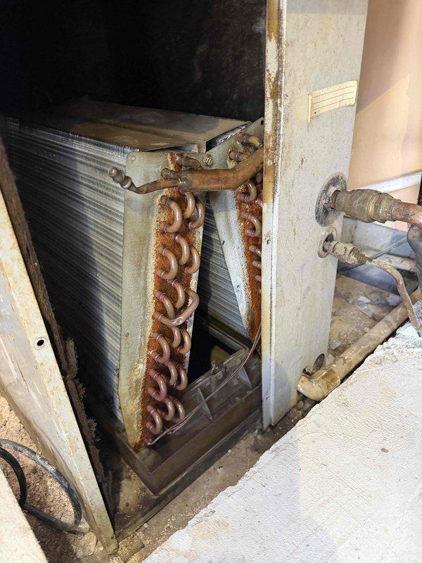 Responded to no cooling complaint at commercial property. Upon inspection, found HVAC unit installed in attic space with severely corroded support chains and mounting hardware showing extensive rust damage. Heat exchanger coil and copper refrigerant lines displayed significant age-related deterioration. Flexible ductwork in attic exhibited discoloration and aging. System components showed advanced weathering inconsistent with proper maintenance, indicating potential structural and operational concerns requiring immediate attention to restore cooling function and ensure safe operation.