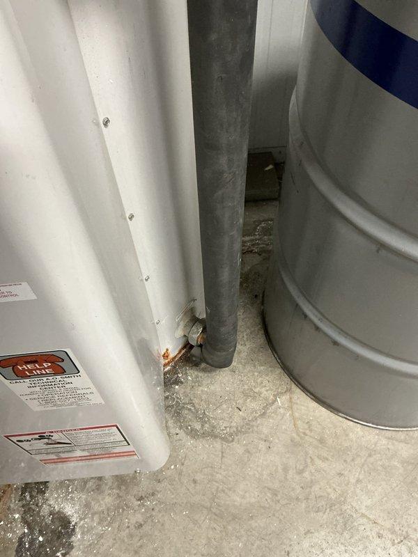 Conducted on-site evaluation of a commercial water heater experiencing leakage from the drain pan in a mechanical room. Assessed the existing white cylindrical water heater unit and surrounding infrastructure, including electrical disconnect switch labeled for electric water heater with proper conduit connections. Documented equipment specifications and spatial constraints in the confined utility area, noting the presence of adjacent cylindrical tanks and limited clearance between components. Provided estimate for complete water heater replacement with a 220-volt unit and step-down transformer as requested to meet the facility's electrical requirements.