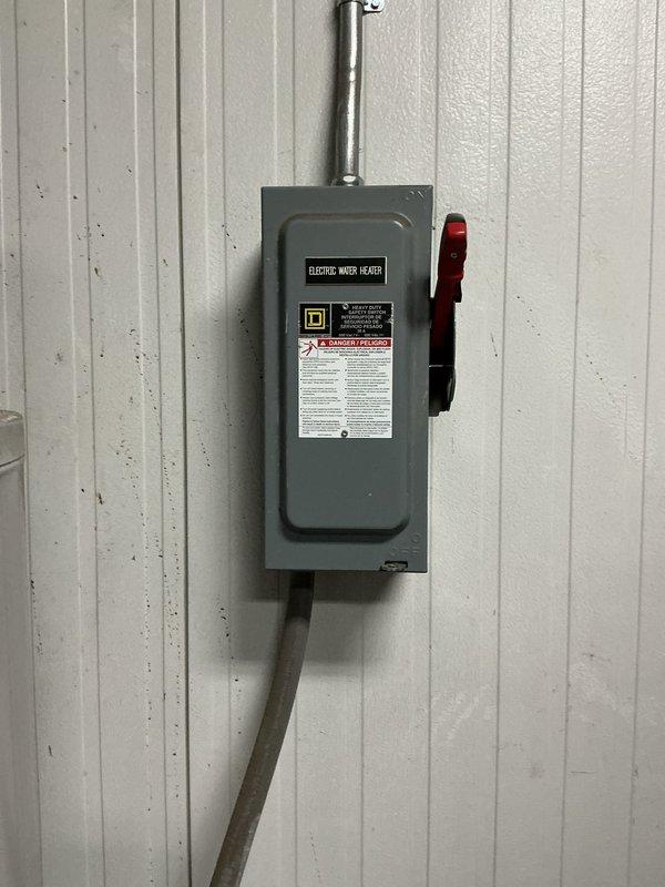 Conducted on-site evaluation of a commercial water heater experiencing leakage from the drain pan in a mechanical room. Assessed the existing white cylindrical water heater unit and surrounding infrastructure, including electrical disconnect switch labeled for electric water heater with proper conduit connections. Documented equipment specifications and spatial constraints in the confined utility area, noting the presence of adjacent cylindrical tanks and limited clearance between components. Provided estimate for complete water heater replacement with a 220-volt unit and step-down transformer as requested to meet the facility's electrical requirements.