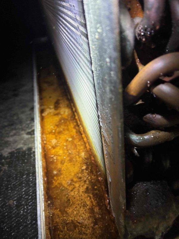 Responded to no cooling complaint on system over 10 years old. Upon inspection, discovered active evaporator coil leak that had been ongoing for approximately one month. Found significant standing water in drain pan with orange-brown discoloration and sediment accumulation, indicating prolonged leakage and possible secondary drain line blockage. Observed substantial mineral deposits and rust-colored buildup around coil base and housing junction. Condensation present on refrigerant lines confirmed system had been attempting to operate despite leak. Documented conditions with photos showing contaminated drain pan, corroded components, and crystallized mineral accumulation on evaporator coil assembly. Advised that evaporator coil replacement would be necessary to restore proper system operation and prevent further water damage to surrounding components and structure.