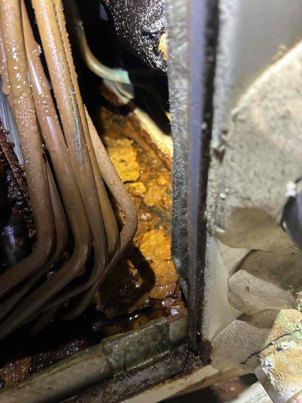 Responded to no cooling complaint on system over 10 years old. Upon inspection, discovered active evaporator coil leak that had been ongoing for approximately one month. Found significant standing water in drain pan with orange-brown discoloration and sediment accumulation, indicating prolonged leakage and possible secondary drain line blockage. Observed substantial mineral deposits and rust-colored buildup around coil base and housing junction. Condensation present on refrigerant lines confirmed system had been attempting to operate despite leak. Documented conditions with photos showing contaminated drain pan, corroded components, and crystallized mineral accumulation on evaporator coil assembly. Advised that evaporator coil replacement would be necessary to restore proper system operation and prevent further water damage to surrounding components and structure.