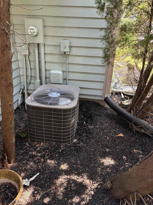 Conducted on-site evaluation of existing residential HVAC system for equipment replacement. Documented current outdoor condensing unit condition, noting tan/beige air conditioning condenser with grid-patterned casing positioned against exterior wall on mulched ground. Assessed electrical service connections including meter, conduit routing, and junction box placement for compatibility with replacement equipment. Measured existing ductwork dimensions, recording 15-19 inch measurements of metal supply plenum and documented copper refrigerant line routing for proper sizing of new system components. Provided comprehensive photographic documentation of current installation to support equipment replacement proposal and ensure accurate system specifications for future installation.