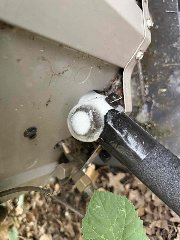 Responded to cooling complaint where thermostat was set to 65°F but reading 76°F despite recent thermostat rewiring in May. Upon arrival, found outdoor condenser unit heavily overgrown with vegetation covering top and front grilles, restricting airflow and preventing proper heat rejection. Discovered frozen refrigerant line with significant ice buildup on suction line coupling near unit, indicating restricted airflow causing evaporator coil to freeze. Cleared all vegetation from condenser unit including vines and ground cover to restore proper airflow. Verified condensate drain line clear and functioning. System airflow restriction from vegetation growth was root cause of inadequate cooling performance and temperature differential issue. Unit operating properly after vegetation removal and allowing sufficient time for ice to melt from refrigerant lines.