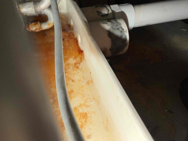 Responded to service call for HVAC unit with reported small leak and suspected condensate drain line backup. Upon inspection, found standing water with rust-colored discoloration in drain pan, indicating drainage system failure. Evidence suggested improper installation methods may have been used on original drain line. Removed existing condensate drain line and installed new PVC drain line with properly configured P-trap to ensure adequate air gap and prevent future backups. Tested drainage system operation and confirmed proper flow and function. Unit drain pan cleared of standing water and system returned to normal operation.