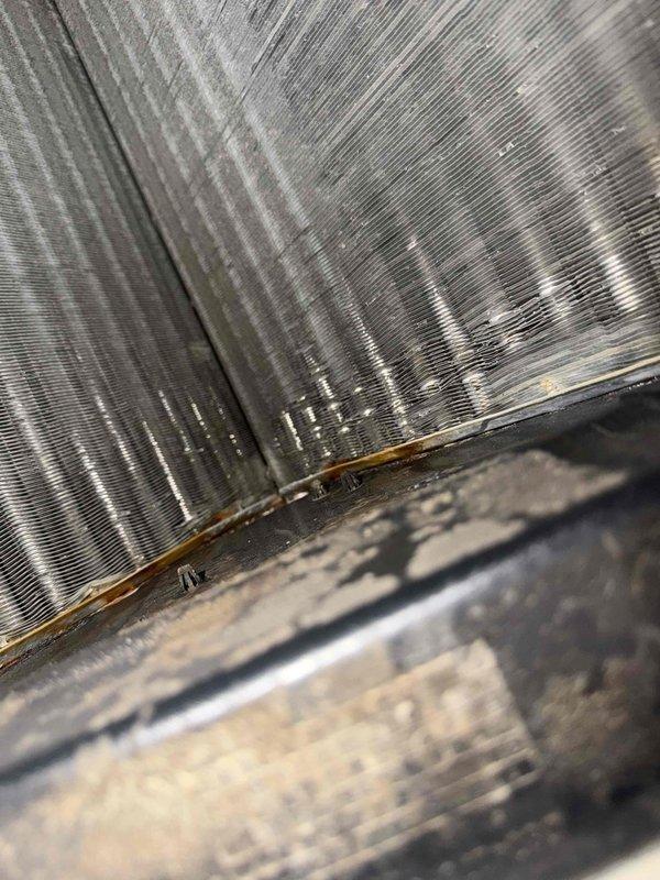 Responded to callback for system freezing issue. Upon arrival, performed thorough inspection of air handling unit and evaporator coil assembly. Found evaporator coil with significant dust and debris accumulation on fins and surrounding components. Drain pan showed heavy buildup of dirt and contaminants, indicating restricted airflow as primary cause of freeze-up condition. Documented coil condition with photos showing corroded areas at coil junction and substantial fouling throughout finned surfaces. Explained findings to occupant regarding need for professional coil cleaning to restore proper airflow and prevent future freezing. System requires coil cleaning service to resolve underlying issue and restore normal operation.