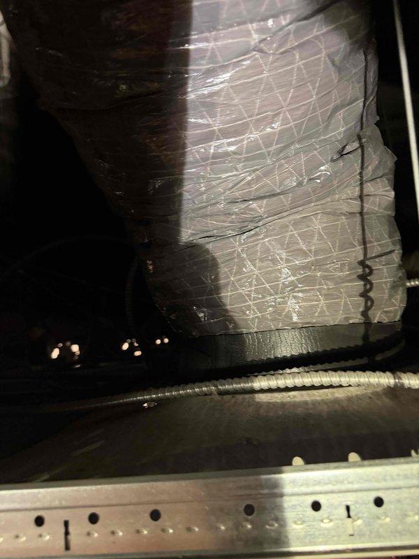 Responded to water leak complaint in boardroom with water dripping from supply vent. Upon inspection, identified inadequate insulation on approximately 12 inches of trunk line and flex duct connection point in plenum space above affected area. Cold air passing through uninsulated ductwork section was causing condensation to form and drip through the supply register. Documented conditions with photos showing compromised insulation material with visible wear, tearing, and dust accumulation on flex duct assembly. Recommended proper insulation restoration of exposed ductwork section to eliminate condensation issue and prevent future water intrusion.