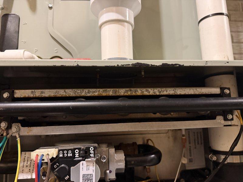 Responded to service call for combustion vent leaking water into HVAC unit. Upon inspection, discovered significant water intrusion through PVC vent piping causing moisture accumulation in drain pan with visible mold and biological growth. Identified compromised vent connection at heat exchanger assembly where condensate was entering system. Assessed corroded internal components including drain pan and metal piping showing deterioration from prolonged water exposure. Documented existing conditions including contaminated surfaces, corroded gas valve area, and compromised drain system requiring attention to prevent further damage to unit.