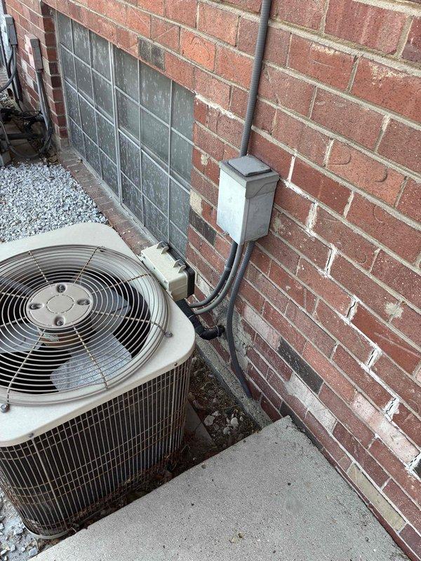 Conducted site assessment for complete HVAC system replacement at residential property. Evaluated existing aged cylindrical condenser unit showing significant weathering and debris accumulation, documented exterior installation configuration including electrical conduit routing and junction box placement, and measured interior refrigerant line spacing to provide accurate equipment specifications and installation requirements for replacement estimate.