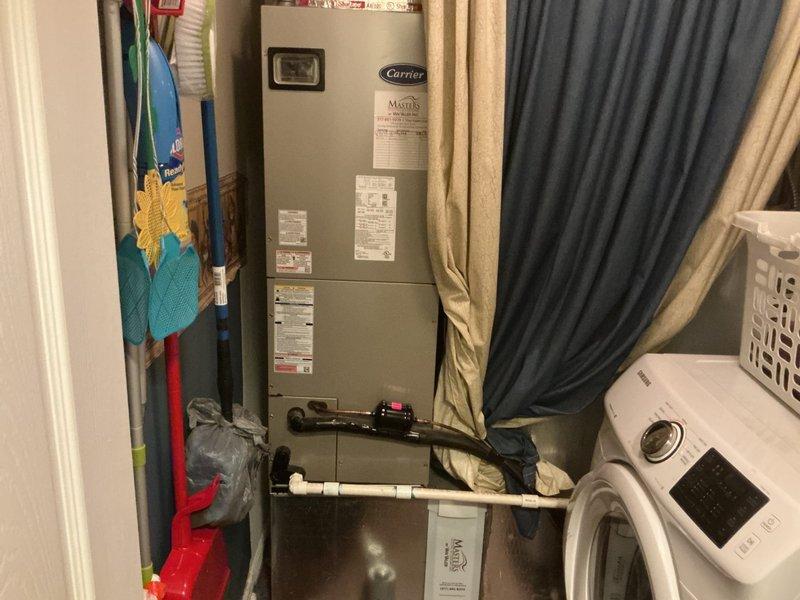 Responded to call for water leak near furnace with significant pooling requiring towels. Upon arrival, inspected Carrier HVAC unit located in utility closet alongside laundry equipment. Examined condensate drain system including white PVC piping running across floor area. Diagnosed source of water leak as blocked or improperly draining condensate line from air handler. Cleared obstruction from drain line, verified proper drainage flow, and tested system operation to ensure leak was resolved. Unit returned to normal operation with no further water discharge observed.