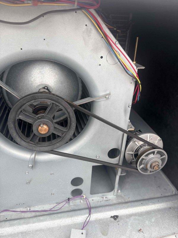 Conducted site survey to document existing HVAC equipment specifications and operational components for maintenance plan proposal. Inspected and photographed belt-driven blower assembly, noting motor configuration, pulley system, and electrical connections within air handler cabinet. Documented filter rack containing four filters in 2x2 configuration, with upper filters showing significant contamination and lower filters appearing recently serviced, indicating varied maintenance intervals across the system.