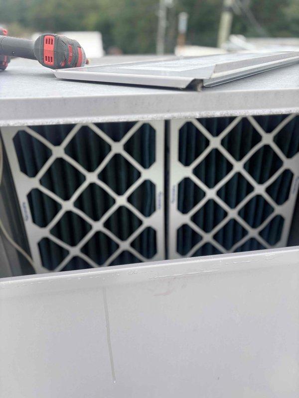 Conducted site survey of commercial rooftop HVAC equipment to document unit specifications and assess condition for maintenance plan proposal. Accessed and photographed rooftop unit mounted on concrete pad, recording manufacturer information, model data, and warning labels from equipment nameplate. Inspected filter assembly and documented equipment configuration, noting surface staining on roof deck near unit base indicating potential drainage concerns that should be monitored during future service visits.