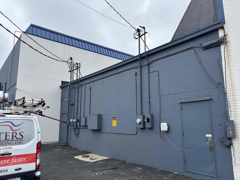 Conducted site survey of commercial facility to document existing HVAC equipment for maintenance plan proposal. Photographed exterior building layout including electrical service components, conduit routing, and rooftop unit locations. Recorded equipment nameplate data and model information from heating unit, capturing access code CRHEATER105A00 and serial numbers for system identification and specification verification.