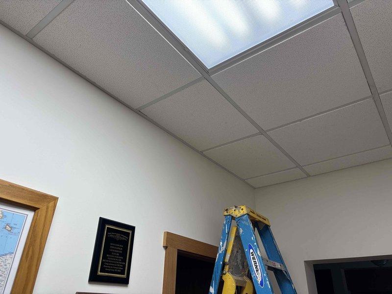 Returned to site to complete miscellaneous work items. Accessed ceiling space via ladder to inspect and photograph drop ceiling system, fluorescent lighting fixtures, and ventilation components. Documented ceiling tile grid layout, recessed light panels, and skylight panel installation for service records.