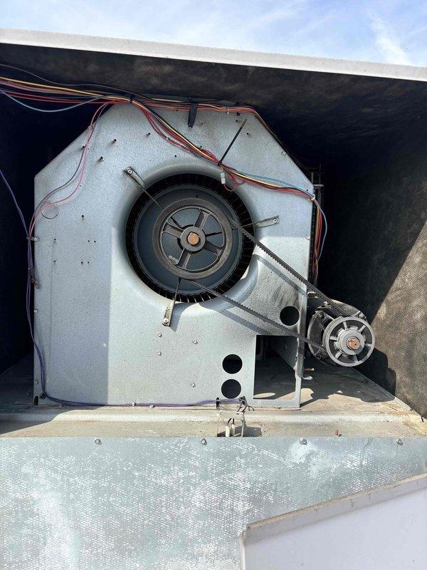 Performed comprehensive inspection of rooftop unit to gather equipment specifications and operational data for preventive maintenance plan development. Documented thermostat settings showing 80-degree setpoint and assessed blower assembly components including centrifugal fan wheel, belt-driven motor system, and housing condition. Photographed all major RTU components to establish baseline equipment inventory and current operating conditions for future maintenance scheduling.