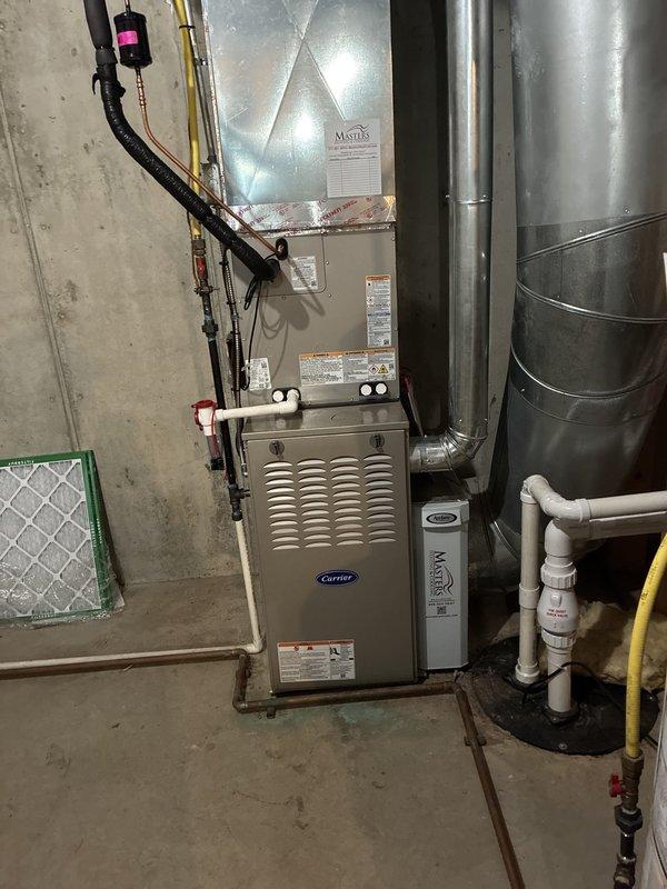Completed full HVAC system installation in basement utility room consisting of Carrier Performance Series equipment. Installed Carrier 26SPA630W003 single-stage air conditioner (16 SEER), Carrier 58TP0B070V17--16 two-stage non-condensing gas furnace (70,000 BTU), and Carrier CVAVA3617XMA evaporator coil. Positioned furnace against concrete block wall with proper clearances and mounted metallic plenum assembly above unit. Connected refrigerant lines using copper tubing with proper brazing techniques and insulation. Installed black flexible gas line to furnace with appropriate fittings and safety shutoff valve. Ran electrical wiring and established proper 24V control circuits between outdoor condensing unit and indoor air handler. Fabricated and installed galvanized steel supply ductwork with secure connections and proper sealing. Installed white PVC condensate drain line with appropriate pitch and trap configuration. Mounted return air filter rack with green frame housing mesh filter me