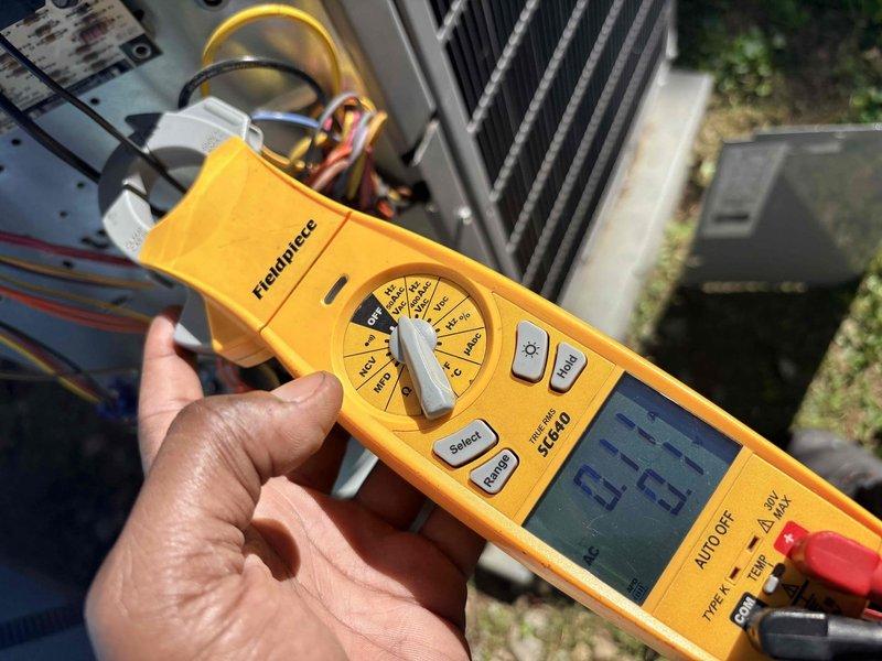 Completed prepaid heating maintenance on residential HVAC system. Performed comprehensive system diagnostics including electrical measurements using digital multimeter, verified proper voltage and amperage readings at outdoor unit, and inspected condenser coil condition. All components operating within normal parameters with system reading 60.5 Hz frequency, refrigerant lines properly connected, and unit cycling correctly.