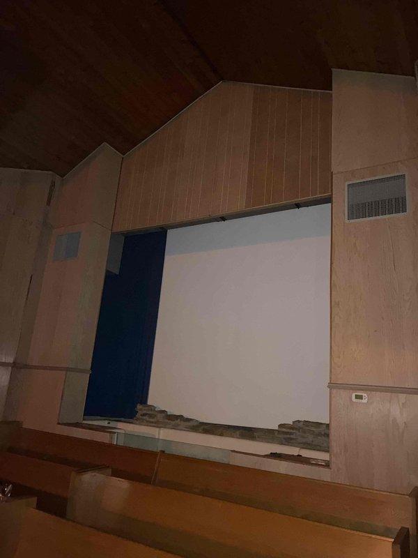 Conducted site assessment of existing HVAC system at church facility to evaluate cooling capacity concerns. Documented exterior ductwork installation showing signs of weathering and rust staining on metal components, and photographed interior auditorium space with wood-paneled walls and exposed beam ceiling to assess current ventilation distribution. Prepared estimate for properly sized commercial cooling equipment replacement based on building volume and occupancy requirements.