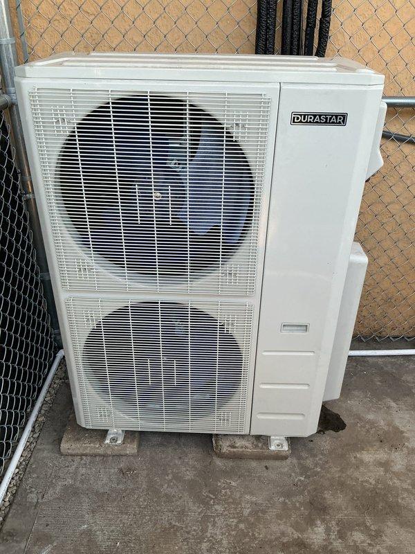 Completed ductless mini-split system installation following resolution of electrical complications. Installed DURASTAR outdoor condenser unit with dual-fan configuration on concrete pad near perimeter fencing, and mounted DURASTAR digital thermostat with programmable controls inside living space. System tested and operational with cooling mode confirmed at setpoint.
