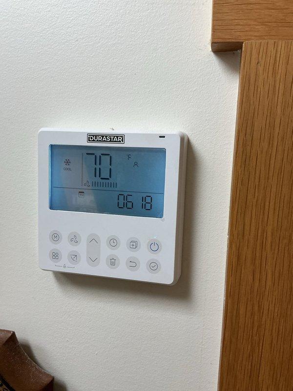 Completed ductless mini-split system installation following resolution of electrical complications. Installed DURASTAR outdoor condenser unit with dual-fan configuration on concrete pad near perimeter fencing, and mounted DURASTAR digital thermostat with programmable controls inside living space. System tested and operational with cooling mode confirmed at setpoint.