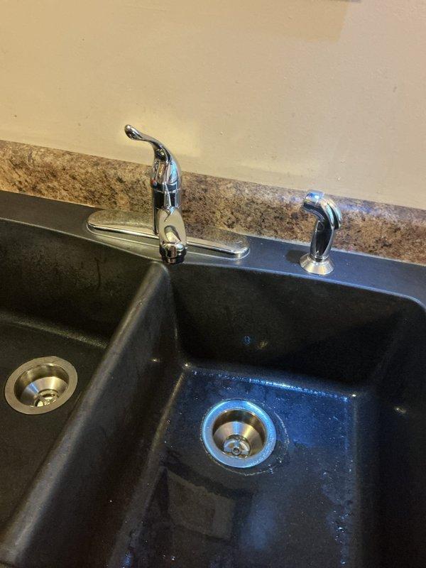 Responded to service call regarding leaking kitchen faucet. Upon inspection, determined existing faucet needed replacement rather than repair. Successfully removed old double-handle chrome faucet and installed new brushed nickel high-arch faucet with side sprayer on granite countertop with double-basin composite sink. Tested new fixture for proper operation and verified no leaks.