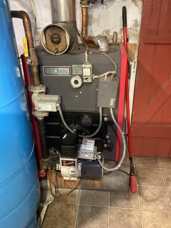 Performed routine maintenance on Crown oil boiler system including nozzle replacement and heat exchanger inspection. System is operating properly, however identified a code violation where vent pipe makes direct contact with wooden structure creating fire hazard. Recommended immediate correction of vent pipe clearance issue to bring installation into compliance with safety standards.
