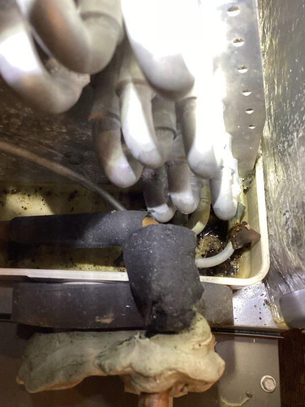 Responded to customer complaint of AC leaking fluid. Inspection revealed significant debris accumulation in the evaporator drain pan causing overflow past the drain line. Removed evaporator cover, thoroughly cleaned debris from pan, and flushed drain line to restore proper drainage. System was tested under operation for an extended period to confirm successful resolution of the leak issue.