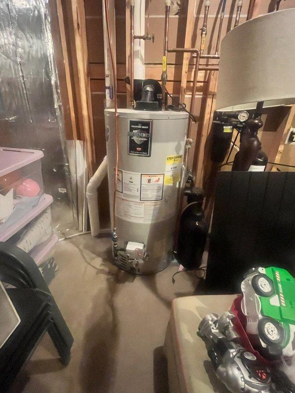 Conducted water heater inspection following customer's report of small water accumulation around unit. Assessed existing water heater with visible "Defender Safety System" and adjacent water treatment system in unfinished utility area. Determined unit requires replacement due to active leak; recommended installation of new water heater with expansion tank under Family Rewards program.