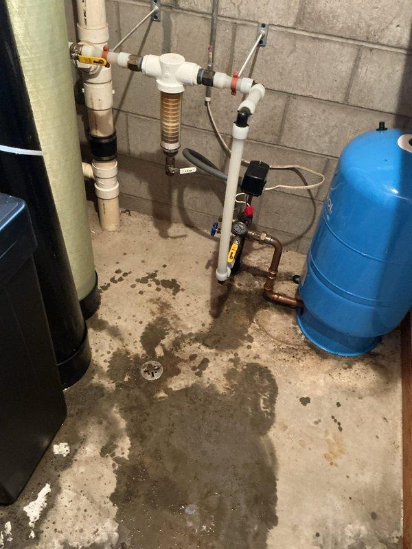 Replaced damaged drain connections on water softener and acid neutralizer that were leaking and causing water accumulation on basement floor. Original softener drain piece was cracked due to over-tightening; ordered replacement part after completing temporary repair to resolve immediate leak issues.